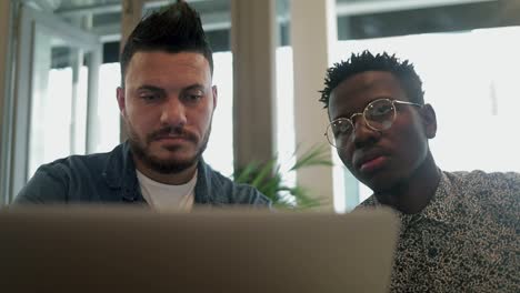 hombres jóvenes concentrados usando computadora portátil en una cafetería