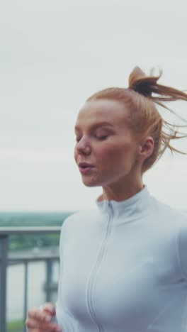 a young woman in active wear focused on her running routine near a scenic view, showcasing determination and physical fitness in an outdoor setting