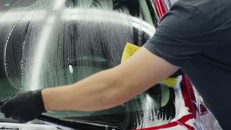 man worker washing red car on a car wash with yellow washcloth.