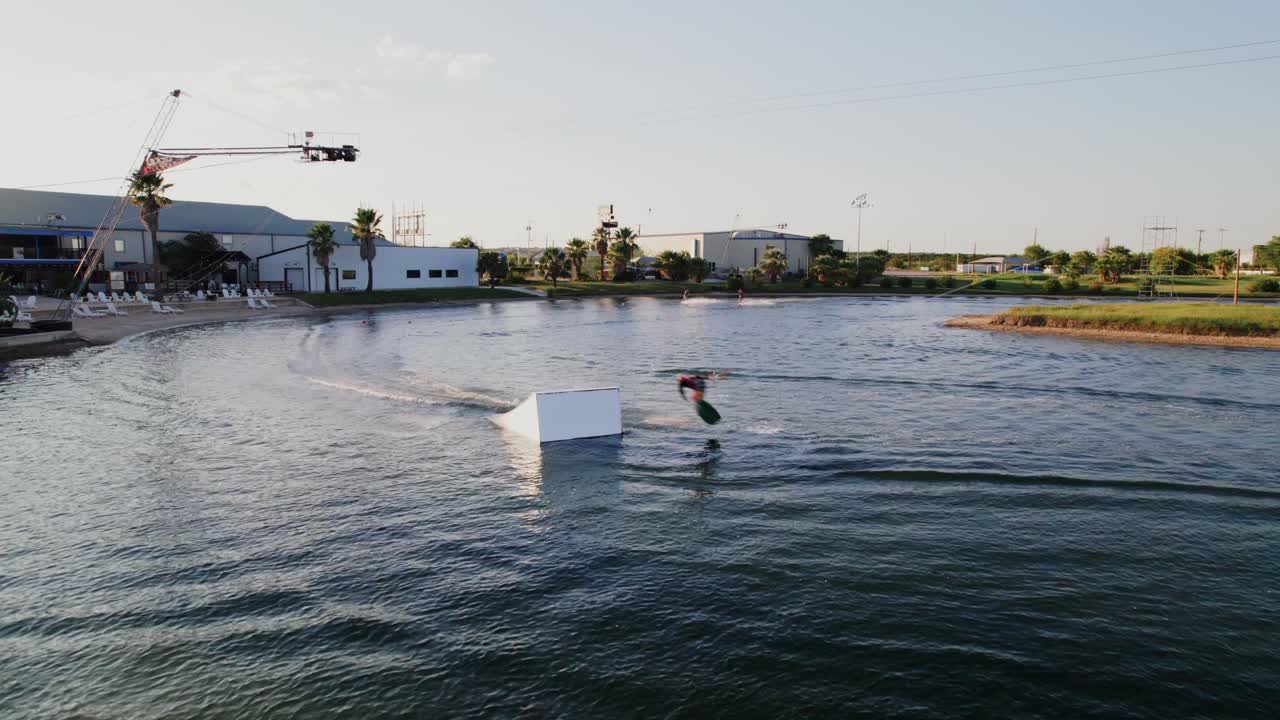 Drone view of someone wakeboarding in the summer sunset, showing off some cool moves on the water