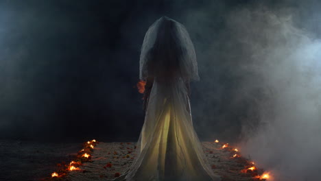 a ghost bride surrounded by candles standing in a dark scary room