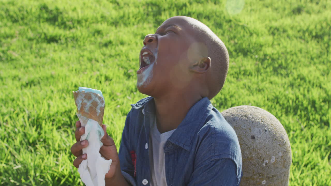Video di un felice ragazzo afroamericano che mangia gelati e ride in una giornata di sole