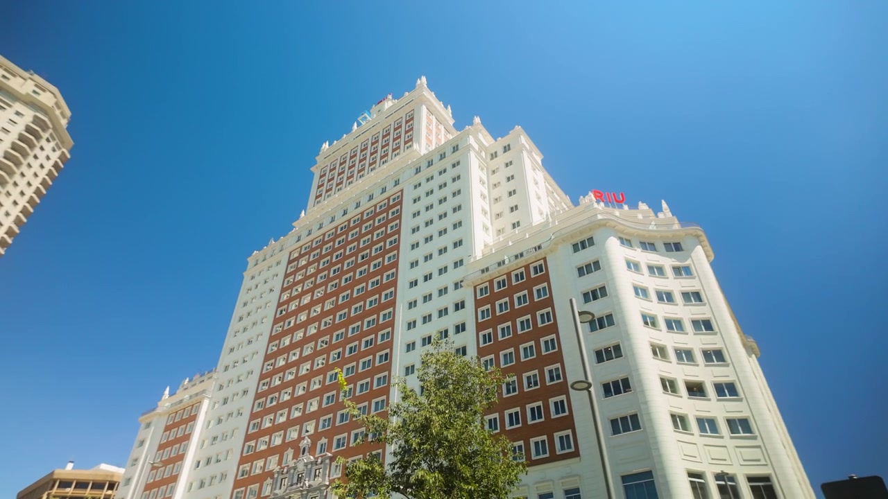 Un plano contrapicado amplio del histórico Edificio España y los rascacielos circundantes en Madrid, España, bajo un cielo azul claro de verano.