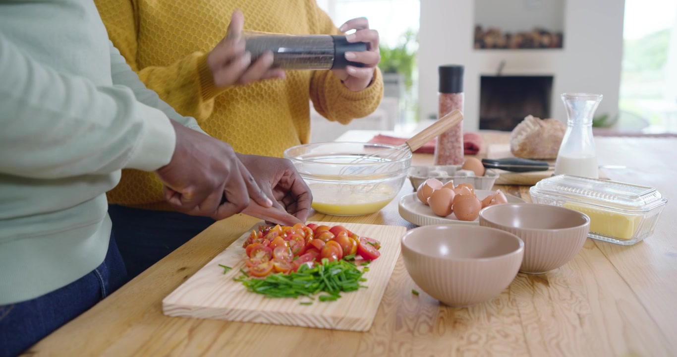 Coppia afroamericana che taglia pomodori in cucina, sbatte le uova mentre il partner macina il pepe