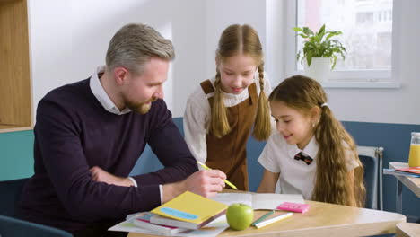 teacher sitting at desk resolving doubts to two female students in english classroom