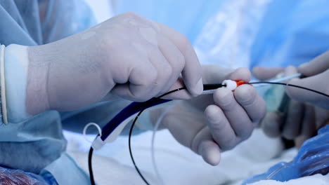 doctor's gloved hands pull the thin black wire from a tube. surgeons using equipment for conducting modern vascular surgery. close up.