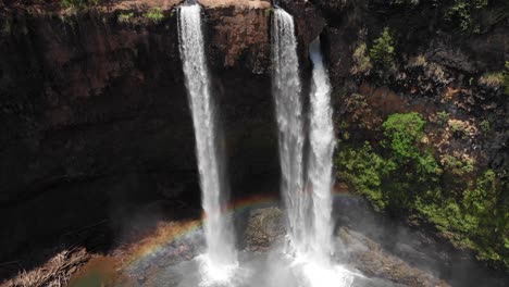 aerial crane shot over wailua falls with beautiful rainbow reflection on the water.