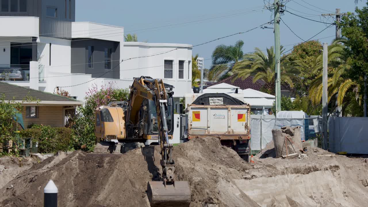 Excavator transfers soil into dump truck on sunny day at modern residential redevelopment site