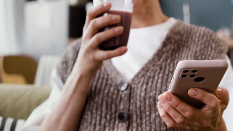 mature woman drinking a smoothie and using her smartphone at home