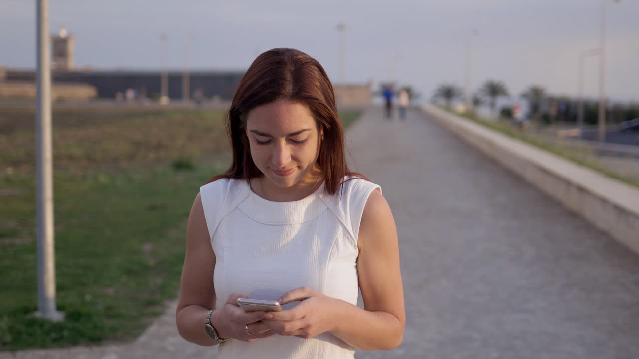 Giovane donna sorridente che usa lo smartphone mentre cammina in un vicolo
