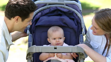 happy parents tending to baby girl in pram in the park