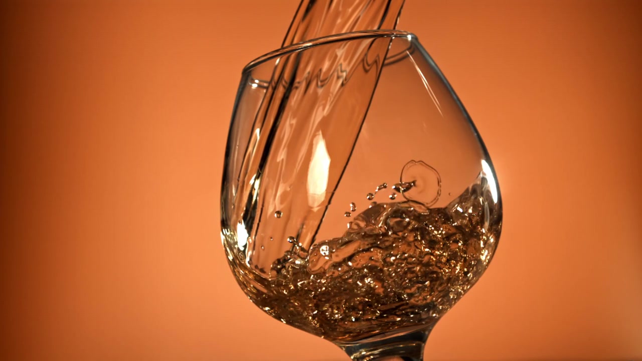 Liquido ambrato dorato che si versa in un bicchiere da cognac al rallentatore
