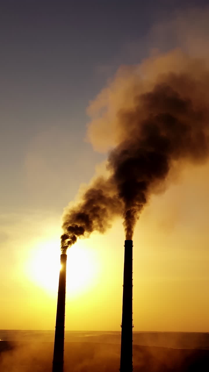 Dark smoke from factory. Industrial pipes of manufacture pollute the atmosphere at sunset. Toxic smoke in the air. Ecological problems. Vertical video