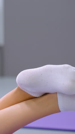 vista trasera de una mujer acostada con las piernas cruzadas en los tobillos, moviéndolas juguetonamente, calcetines blancos en contraste con la alfombra de yoga púrpura, luz de anillo visible en el fondo