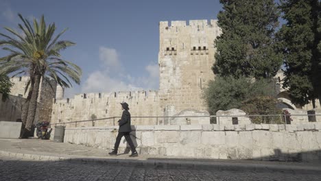 orthodox jew carrying a book walking in front of tower of david in the old city of jerusalem, israel