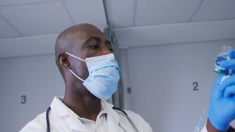 african american male doctor wearing face mask filling the syringe with covid-19 vaccine at hospital