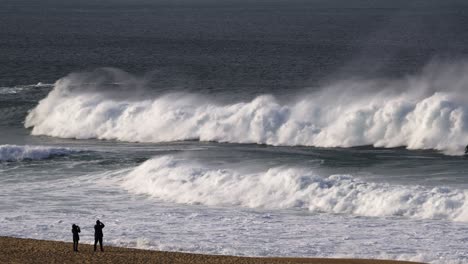 deux personnes sur une plage de sable regardant de grandes vagues de la mer montante