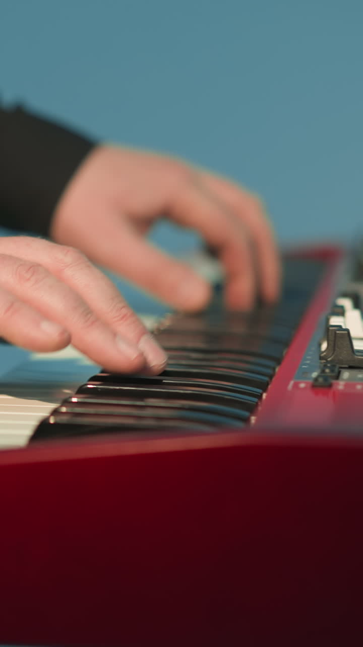 tecladista sin rostro tocando un piano de muestra rojo contra un fondo azul. el primer plano destaca las manos del músico en las teclas
