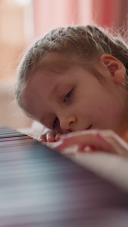 tired junior schoolgirl with plaits presses piano keys leaning on instrument in living room. little child bored of music lesson at home. creative hobby