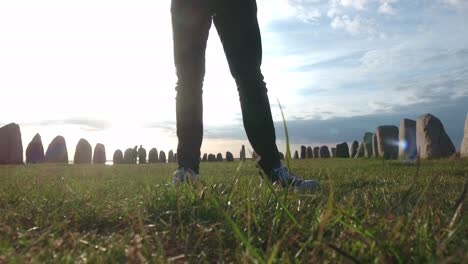 piernas masculinas con jeans negros y conversar de pie frente a ales stenar al atardecer en el verano, sur de suecia skåne österlen kåseberga, estática