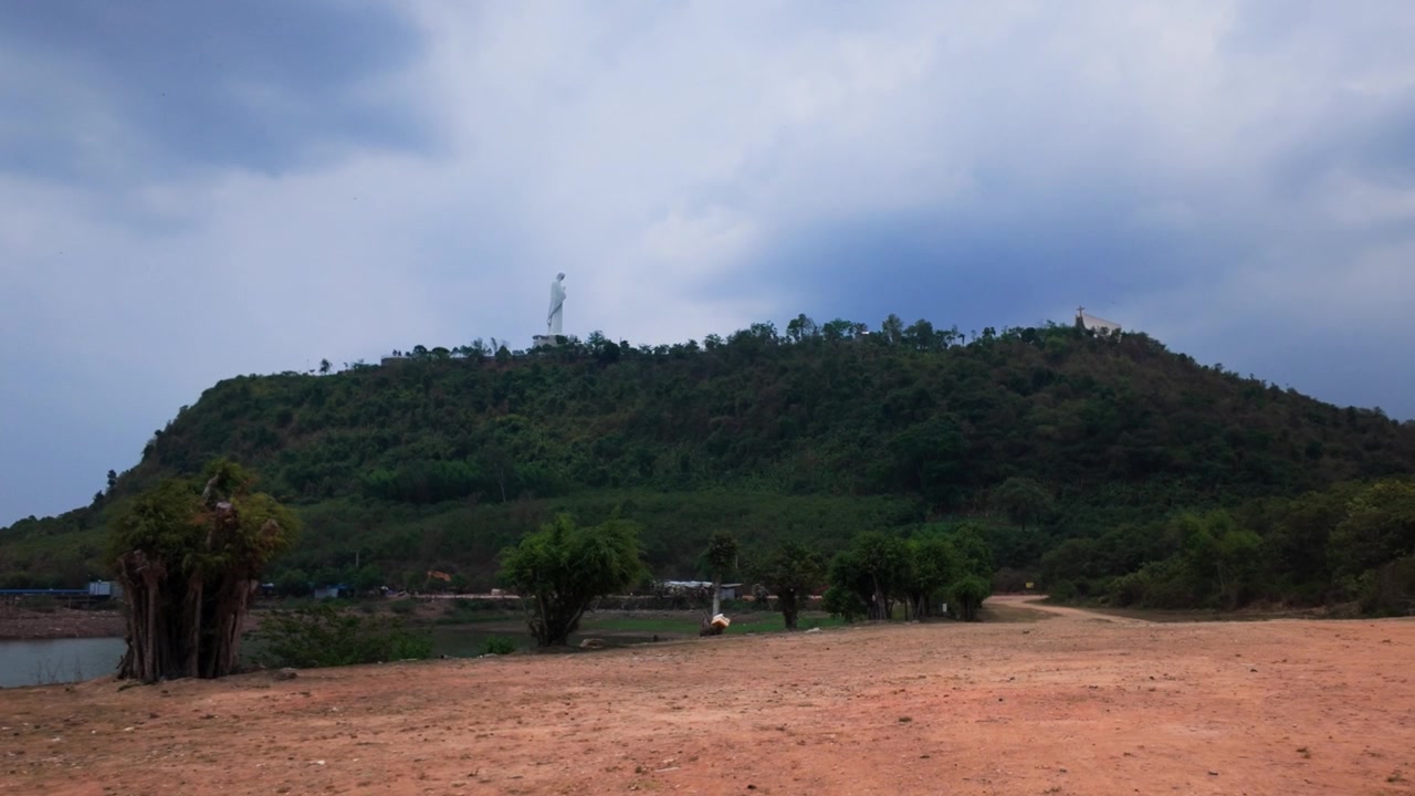 Gåtur langs bredden af Tri An-søen i Dong Nai, Vietnam, hvor folk nyder udsigten til bakkerne. Mørke skyer trækker ind og ændrer himlen. Scenen viser et naturligt landskab