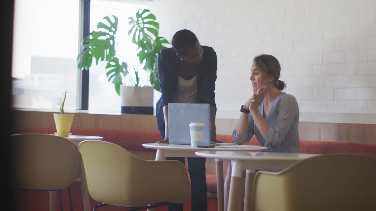 dos colegas femeninas diversas mirando la computadora portátil y discutiendo en un café