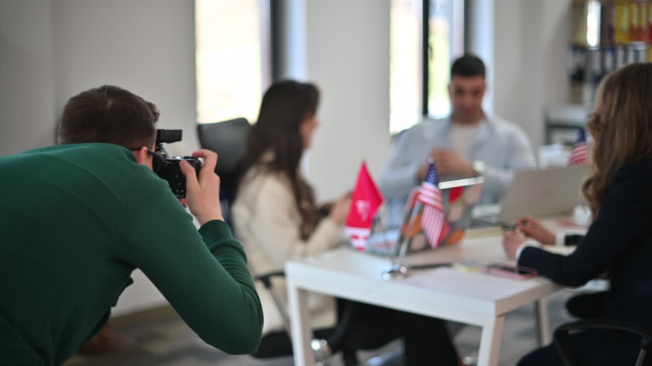 Fotograf som tar bilder av kolleger som snakker ved et skrivebord på et kontor