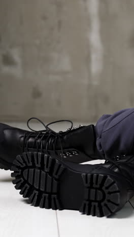 model in grey sportive pants sitting on the white floor in studio. female touching the tongues of black stylish army boots on her feet. vertical video