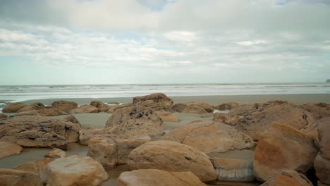 handheld orbiting shot of boulders on the beach in new zealand during the day