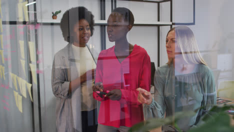 tres mujeres de negocios diversas haciendo una lluvia de ideas con notas en la pared de vidrio de la oficina