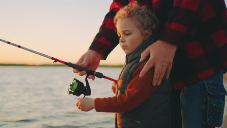 curly little boy is learning to fishing by rod careful father or grandpa is helping happy childhood moments