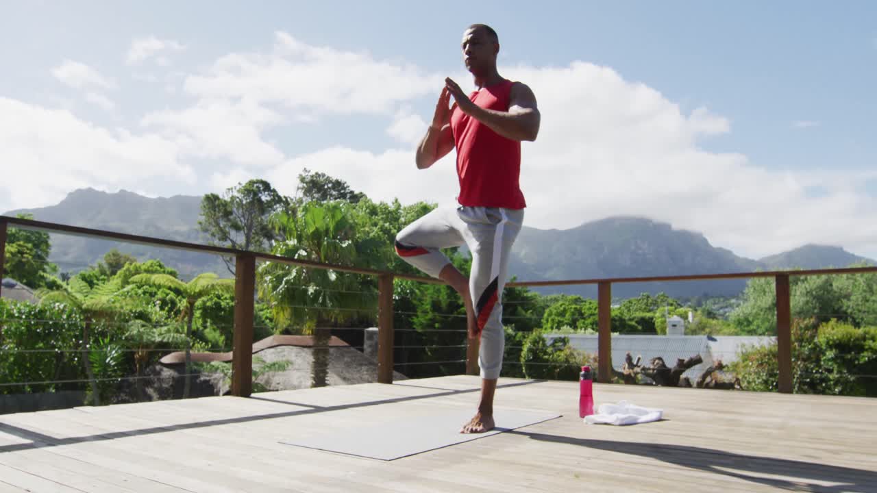 Focused biracial man practicing yoga on mat on terrace