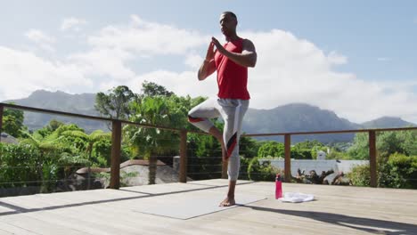 Focused-biracial-man-practicing-yoga-on-mat-on-terrace