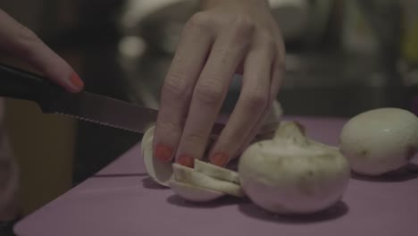 el primer plano de una cocinera está cortando champiñones en cámara lenta en una tabla de cortar