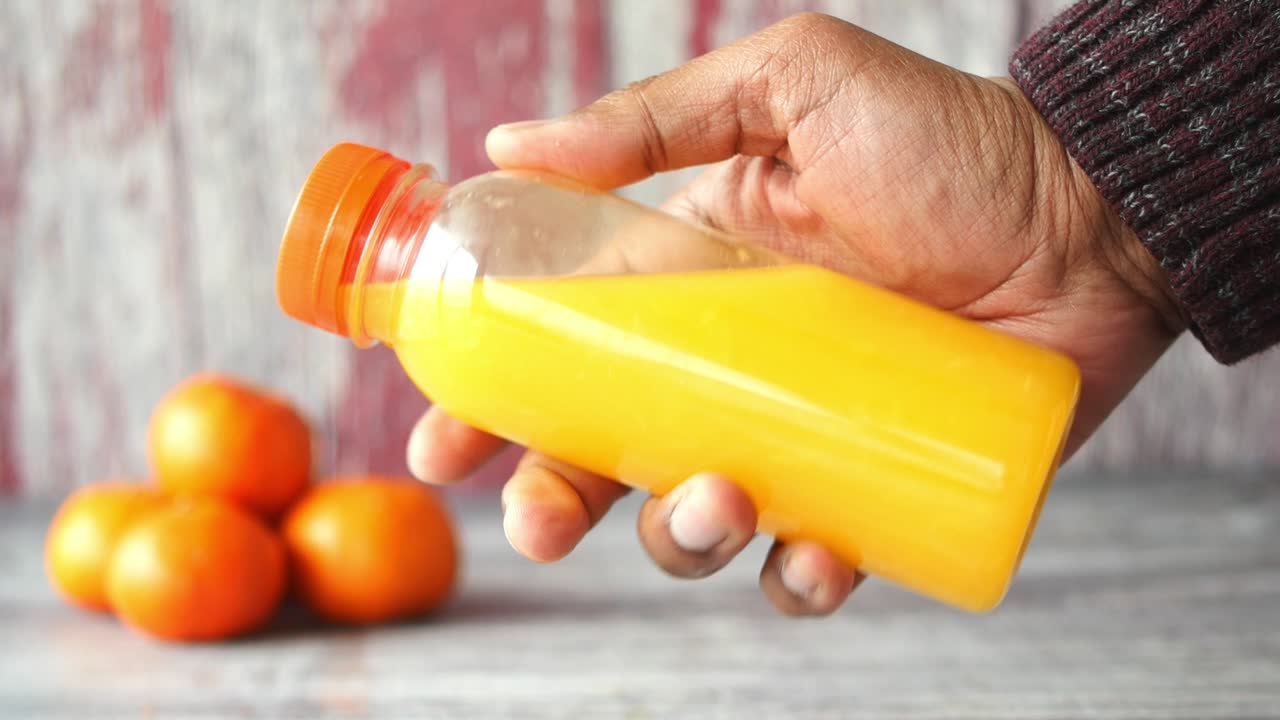 Hand holding a bottle of orange juice with oranges in the background