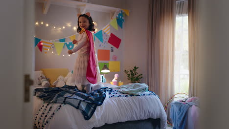 niña feliz saltando en la cama vistiendo disfraz jugando a un juego disfrutando de la imaginación juguetona en un dormitorio colorido en casa