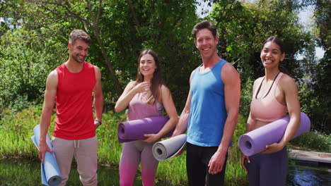 retrato de un grupo diverso sonriente con esteras enrolladas reuniéndose para una clase de yoga al aire libre
