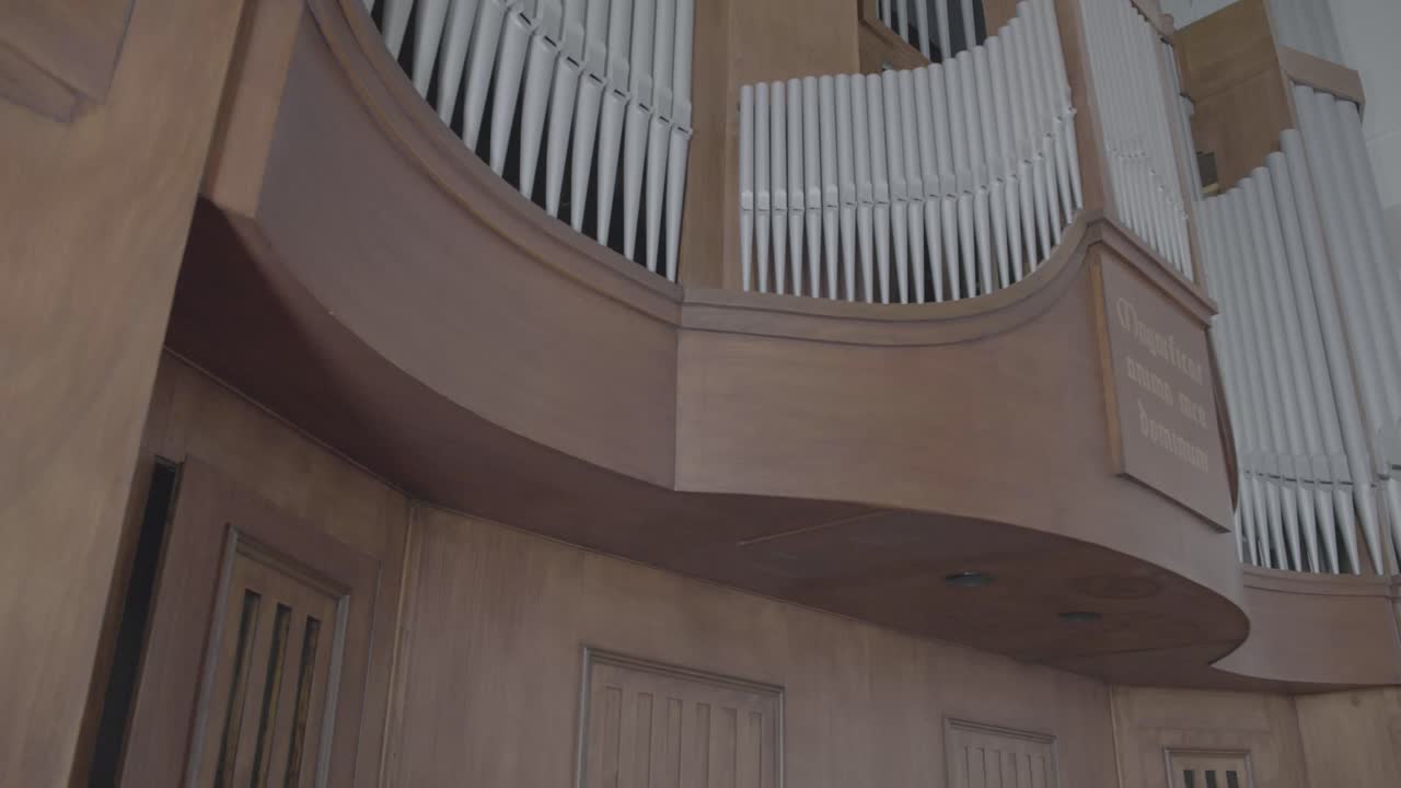 Camera pans along a large organ in the gallery of a church, many organ pipes in the front