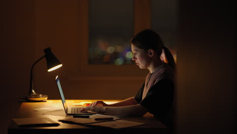 Young-good-looking-Caucasian-woman-typing-and-working-on-the-laptop-computer-as-freelancer-while-sitting-at-home-in-the-cozy-dark-living-room-with-a-cat.-At-night.-Stay-home