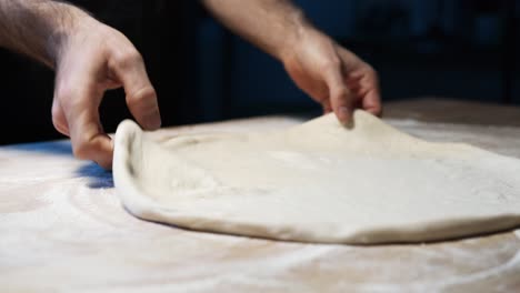 a close-up of a skilled chef's hands put pizza dough on the wooden counter, shallowing it and set it up for the oven