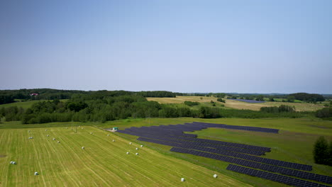 aerial landscape of a small solar panels farm and hay bales in plastic wraps on a field after harvesting crops