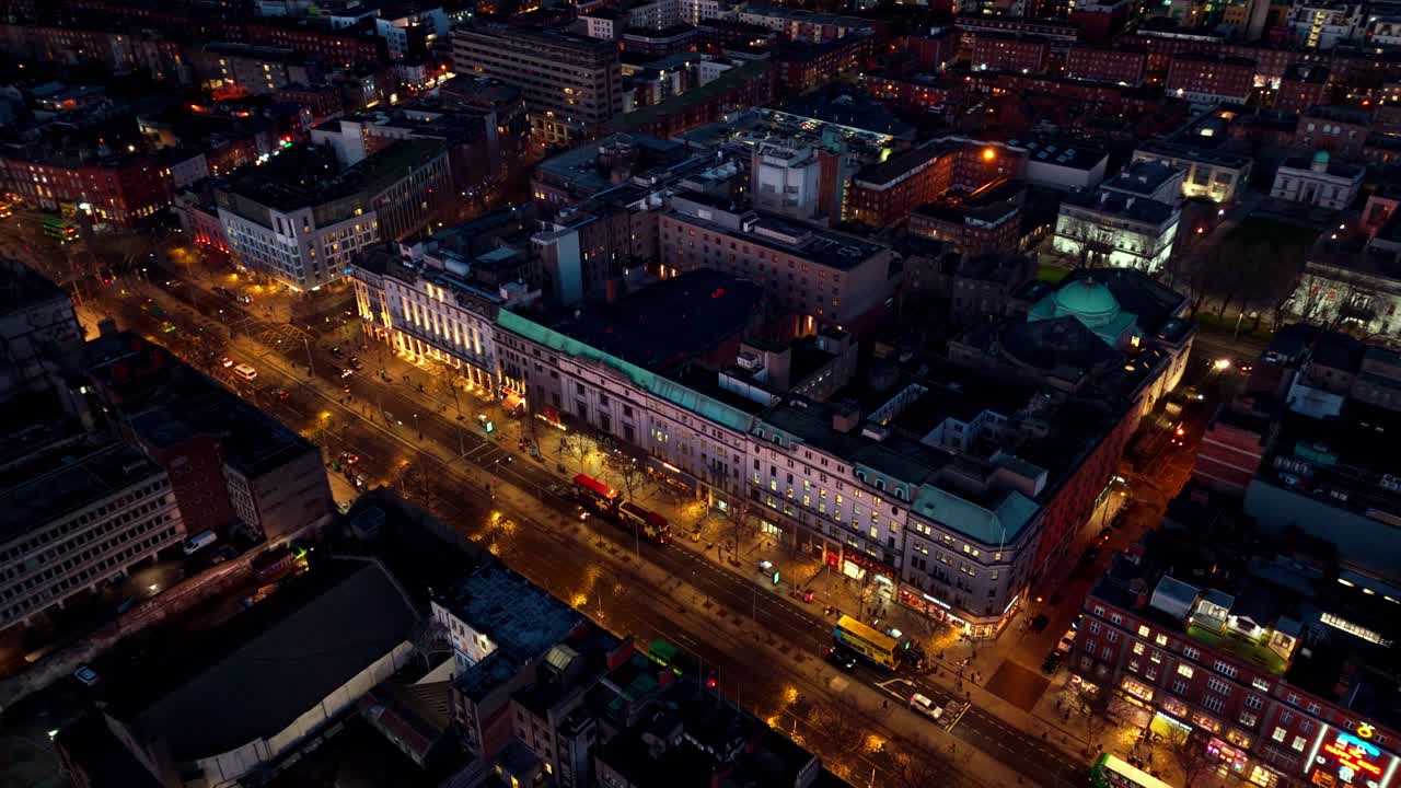 aerial landscape drone shot over O'Connell street in Dublin Ireland with lit street at winter night time and Irish cityscape buildings and cars and tourists on busy road below exploring the streets