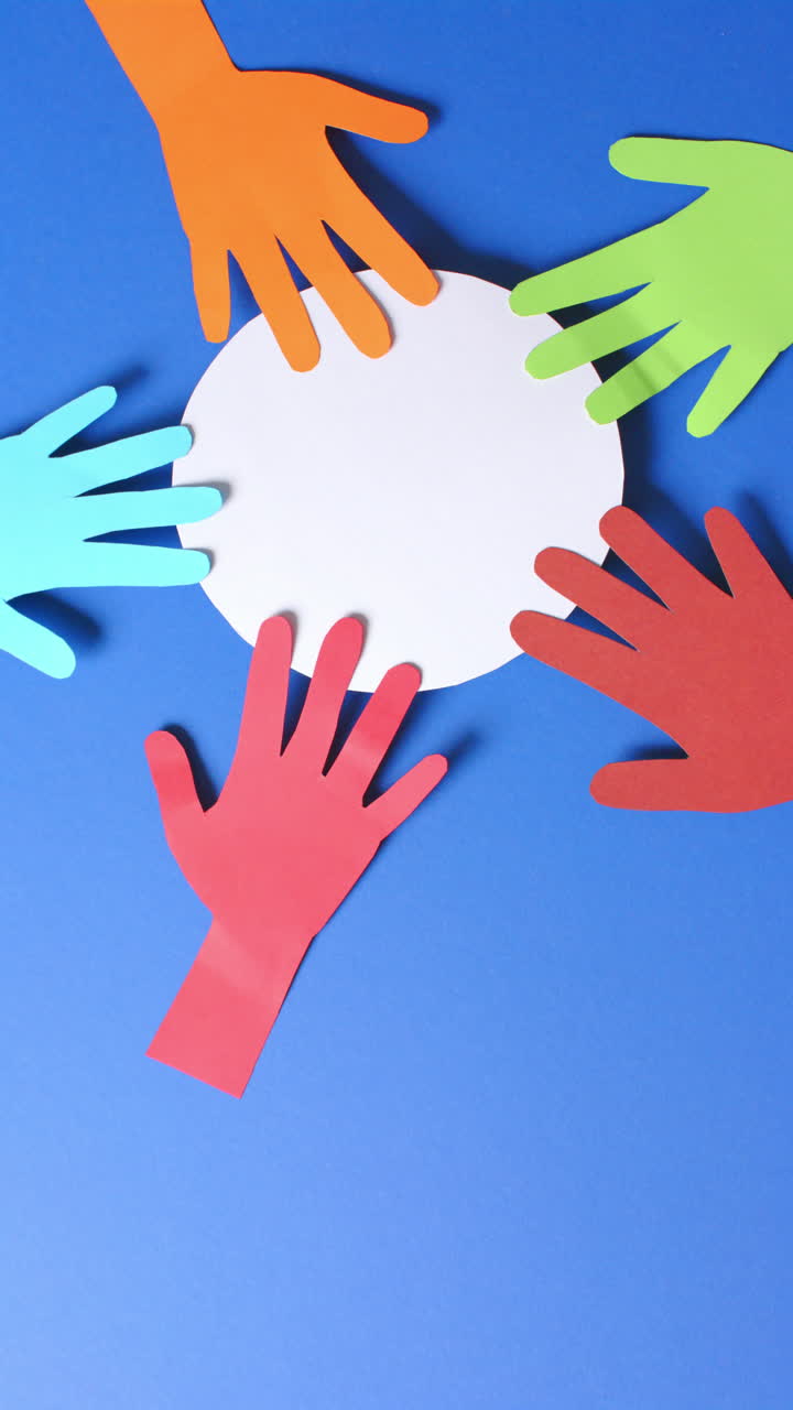 Vertical video of hands touching circle made of colourful paper on blue background with copy space