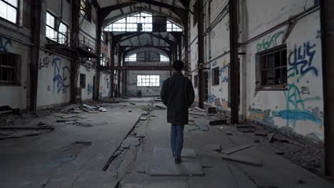 urban explorer navigating sprawling abandoned factory interior, revealing weathered graffiti covered walls, broken windows casting dramatic shadows across decaying industrial space