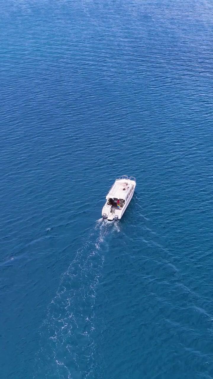 Toma de dron cenital sigue a una lancha motora blanca dejando una estela a través de tranquilas aguas oceánicas tropicales.