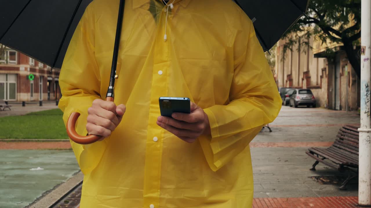 Unrecognizable man standing on the city streets under umbrella and using cellphone. High quality 4k footage