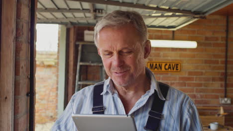 mature male wearing overalls using digital tablet in garage workshop