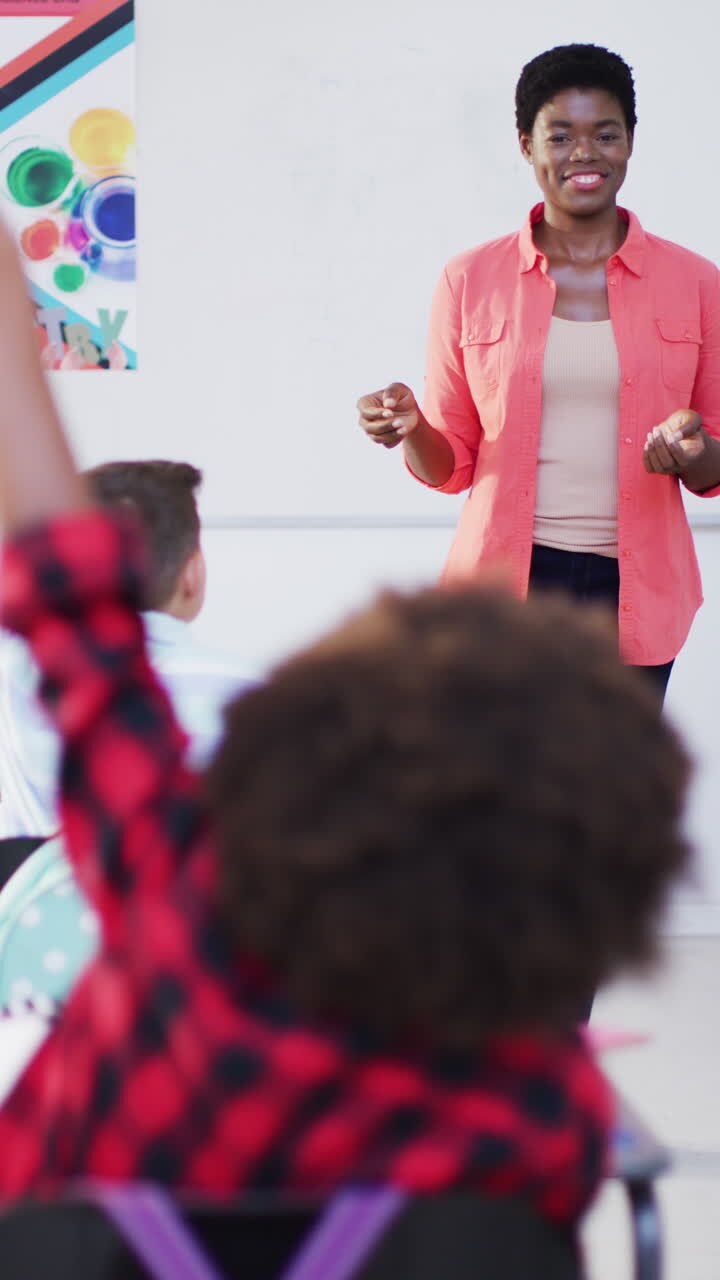 Vertical video of happy diverse female teacher and schoolchildren in school classroom