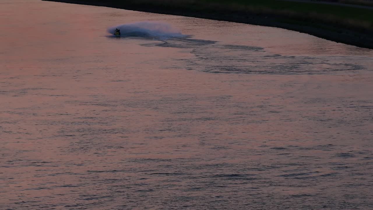 Silhouettes of two people on a jet-ski as one falls off