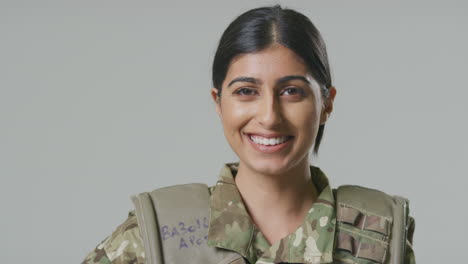 Retrato-De-Estudio-De-Una-Joven-Soldado-Sonriente-Con-Uniforme-Militar-Sobre-Fondo-Liso